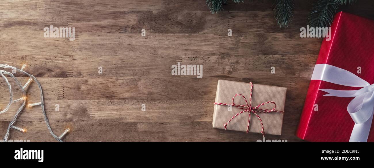 Natale e nuovo anno di sfondo con scatole regalo, luce stringa e decorazioni di pino verde su tavola di legno banner vista dall'alto con spazio copia Foto Stock