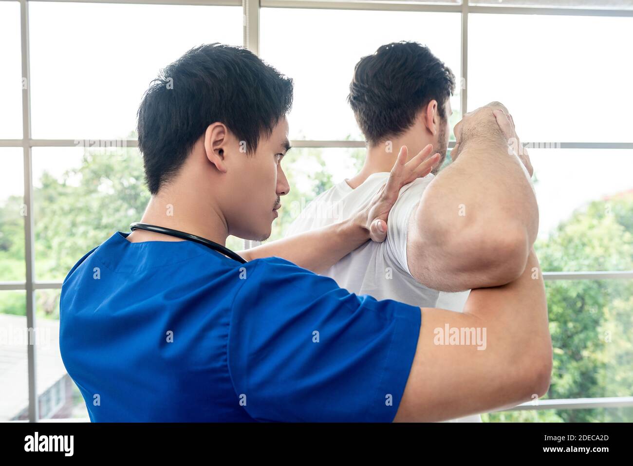 Fisioterapista asiatico che stretching atleta paziente maschile spalla e braccio in clinica Foto Stock