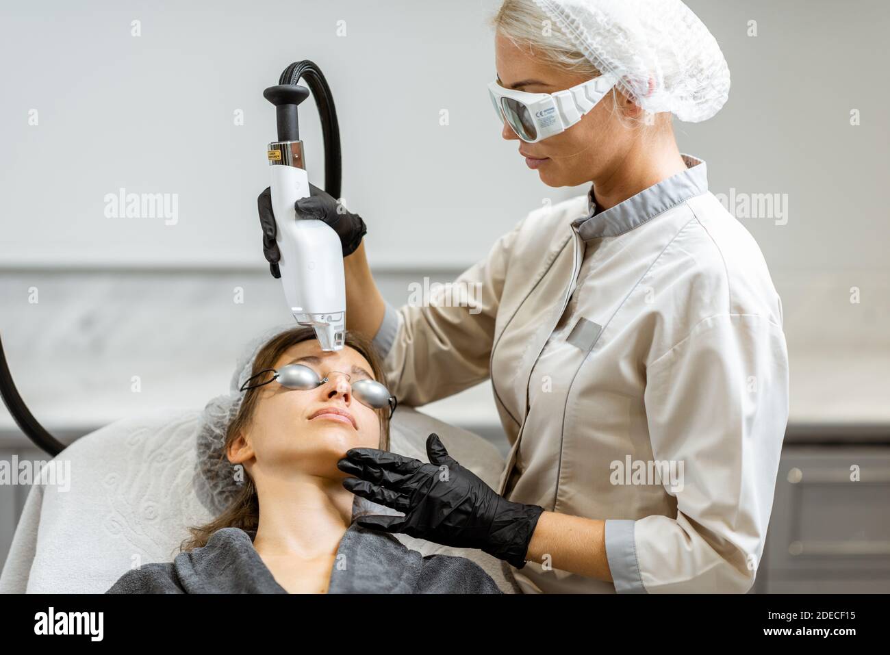 Medico professionista in abbigliamento protettivo che fa un trattamento di ringiovanimento laser per una giovane donna cliente presso l'ufficio medico. Procedura LaseMd Foto Stock