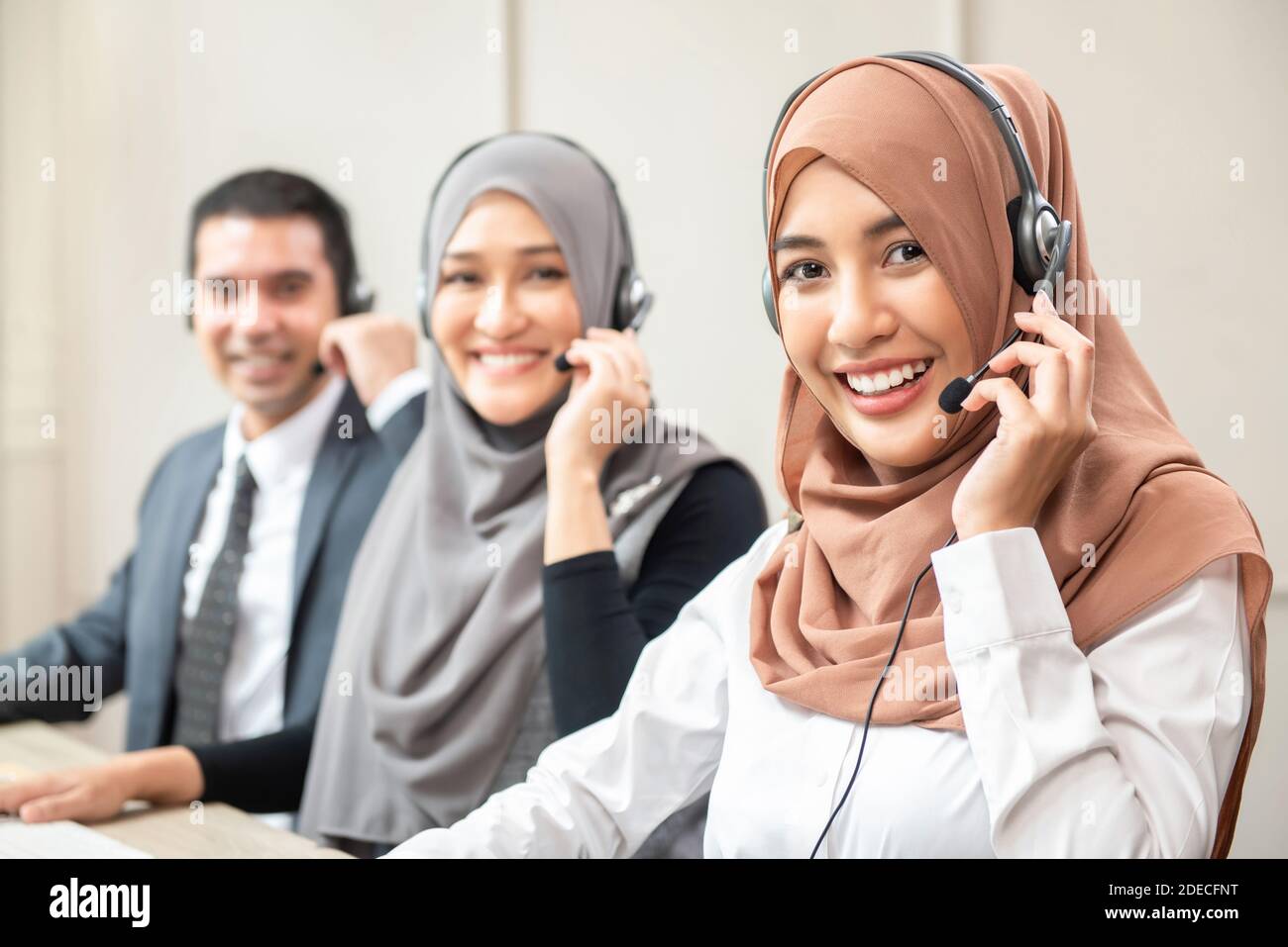 Sorridenti donne musulmane asiatiche che indossano cuffie con microfono che lavorano come clienti operatori sanitari con team presso l'ufficio del call center Foto Stock