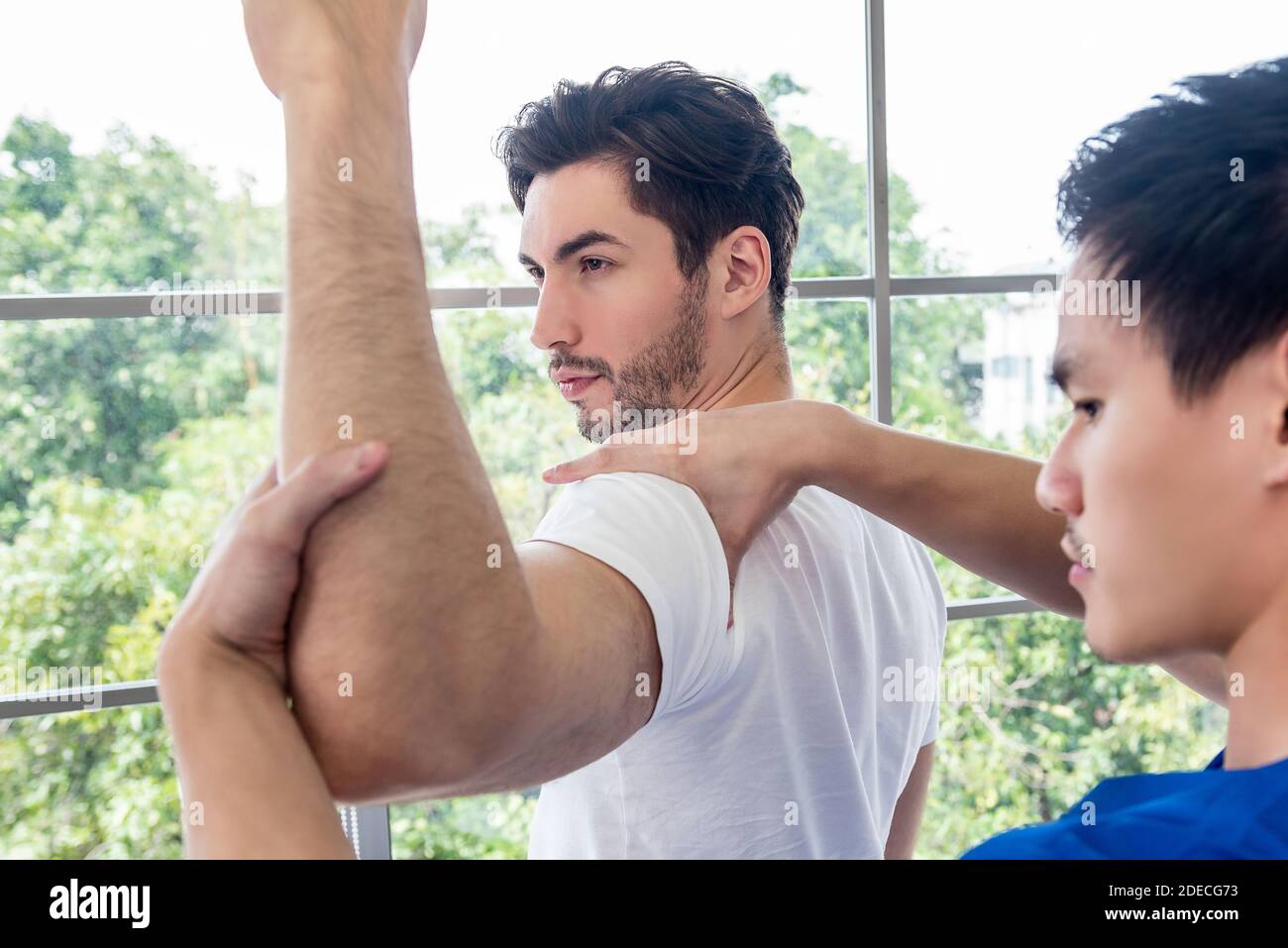 Fisioterapista che massaggiano e stretching atleta spalla paziente maschile e braccio in clinica Foto Stock