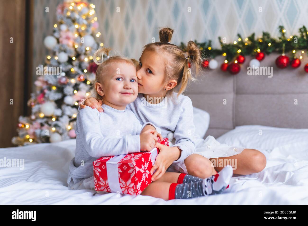 Due sorelle carine ragazze con regali di Natale sedersi a letto a casa in  camera decorata di Natale. La ragazza abbracciò e baciò la sorella Foto  stock - Alamy