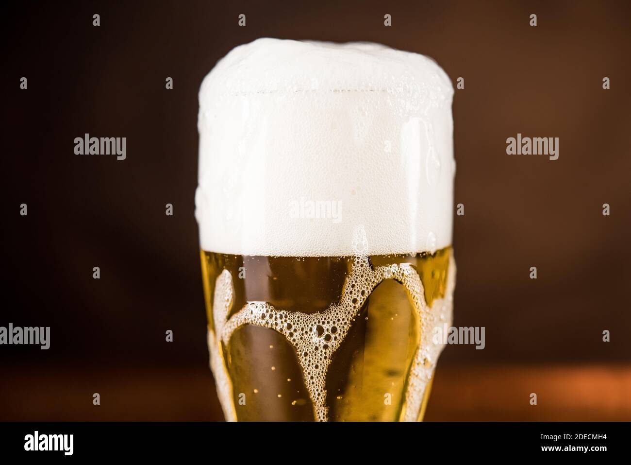 Birra fredda dorata nel bicchiere sul tavolo con schiuma schiumosa a flusso eccessivo Foto Stock