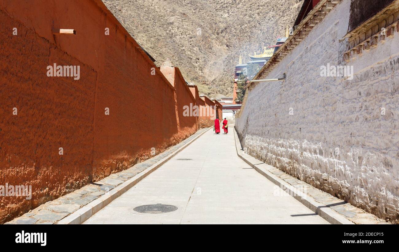 Xiahe, provincia di Gansu / Cina - 28 aprile 2017: Vista lungo un vicolo al monastero di Labrang. A distanza si vestirono due monaci tibetani dell'ordine dei Gelug Foto Stock