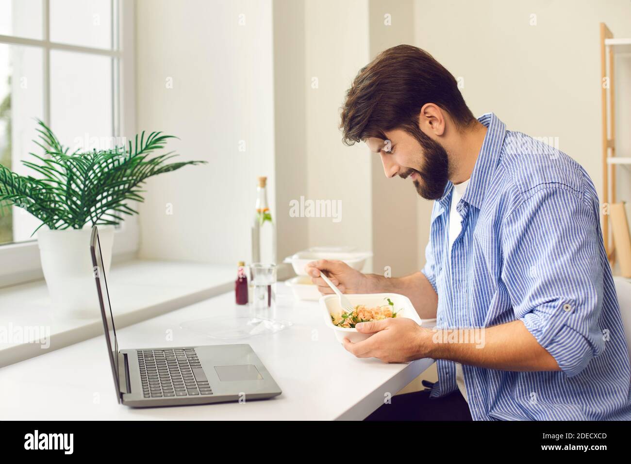 Un giovane impegnato a mangiare cibo da asporto durante la pausa pranzo a casa o in ufficio Foto Stock