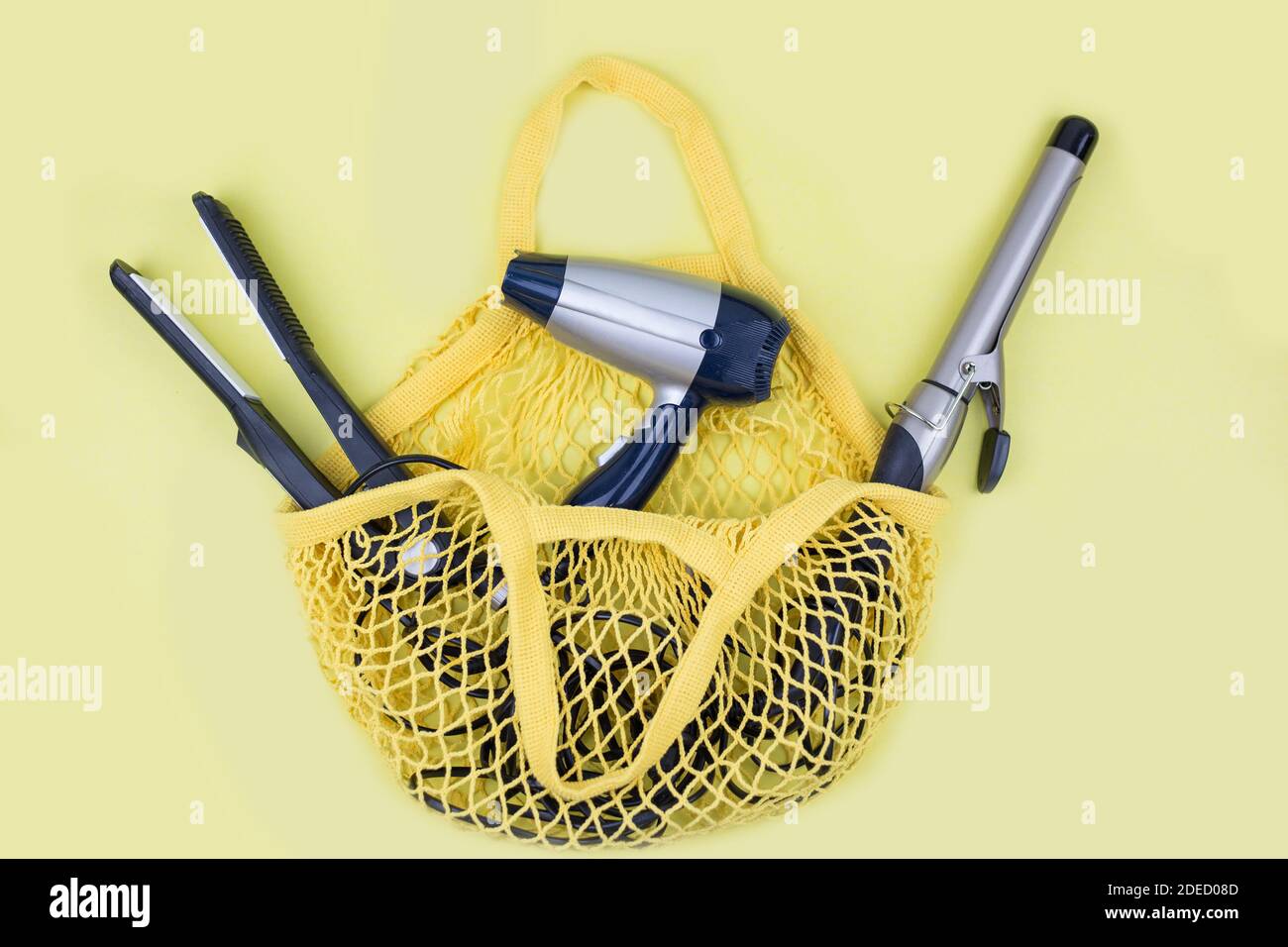 ferro arricciacapelli, asciugacapelli e piastra per capelli sono in una borsetta gialla. Borsa per la spesa con articoli da parrucchiere Foto Stock