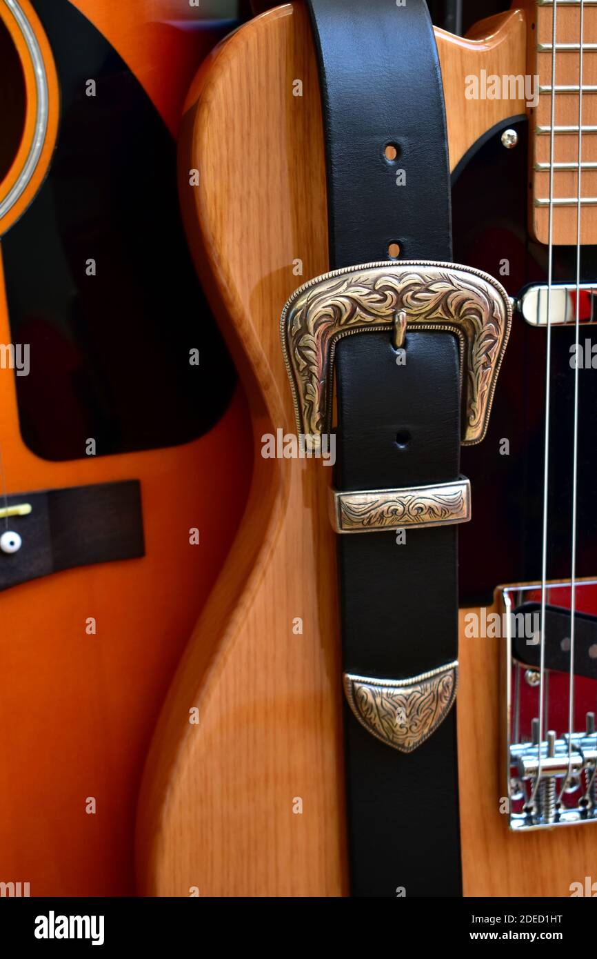 Chitarre acustiche ed elettriche e cinturino in pelle con fibbia in argento da vicino. Foto Stock