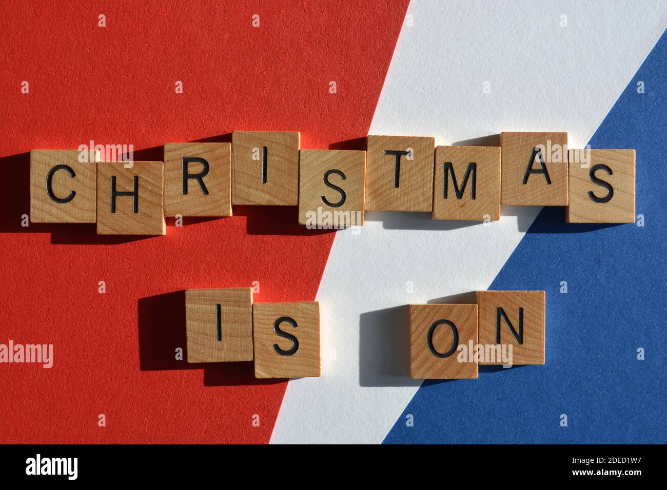 Natale è in corso, parole in lettere alfabetiche in legno isolato su sfondo rosso, bianco e blu Foto Stock