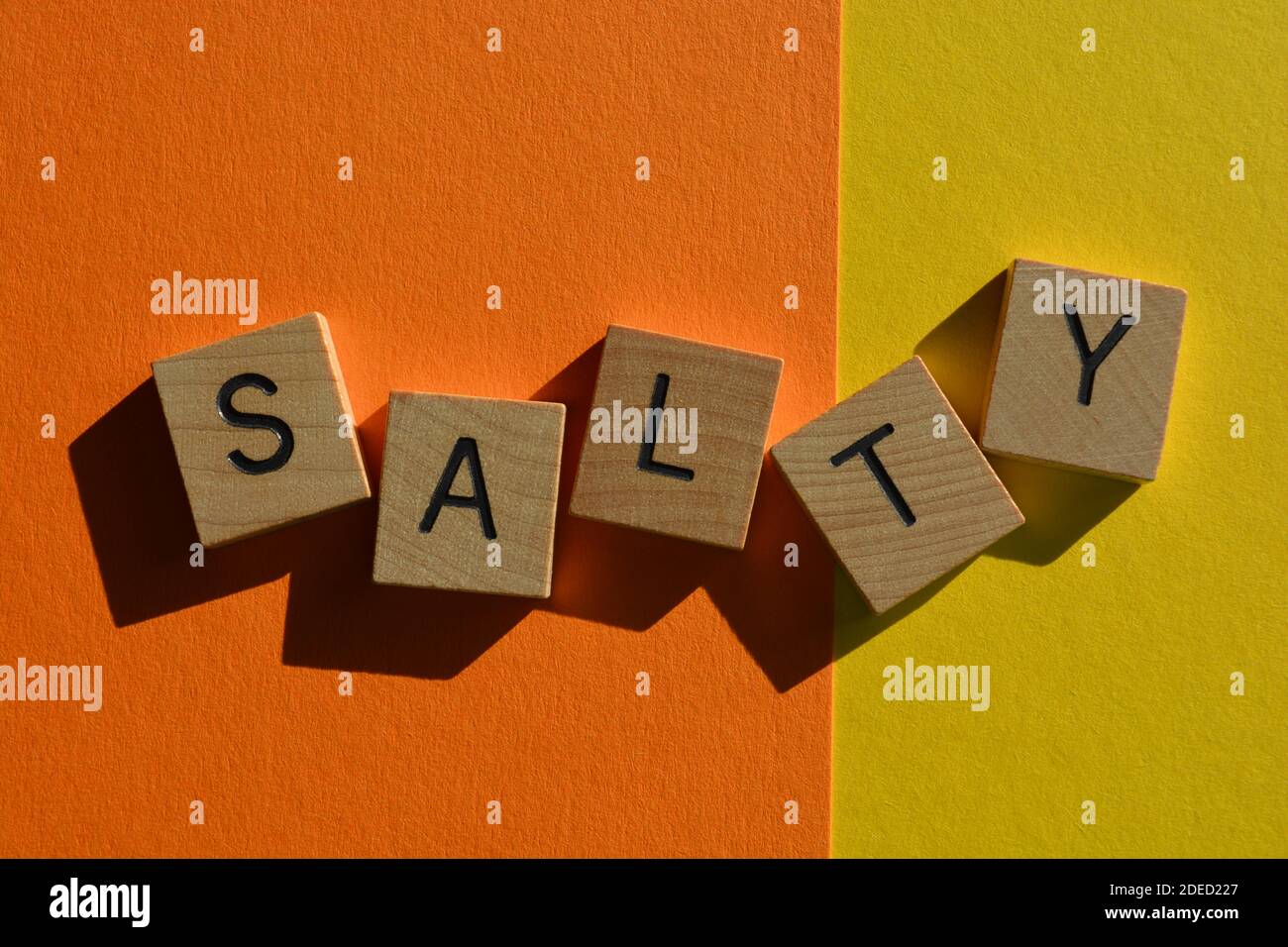 Salato, parola in lettere alfabetiche in legno isolato su sfondo giallo chiaro e arancione Foto Stock