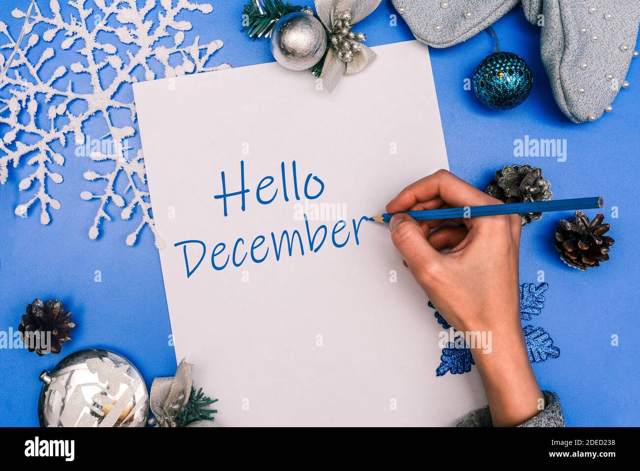 Ciao dicembre. La mano della ragazza scrive il testo su un foglio bianco di carta. Composizione di Natale. Foto Stock