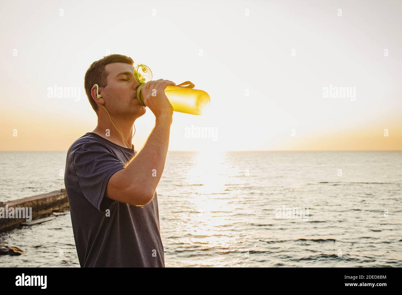 Uomo che beve acqua dalla bottiglia dopo il jogging vicino il mare Foto Stock