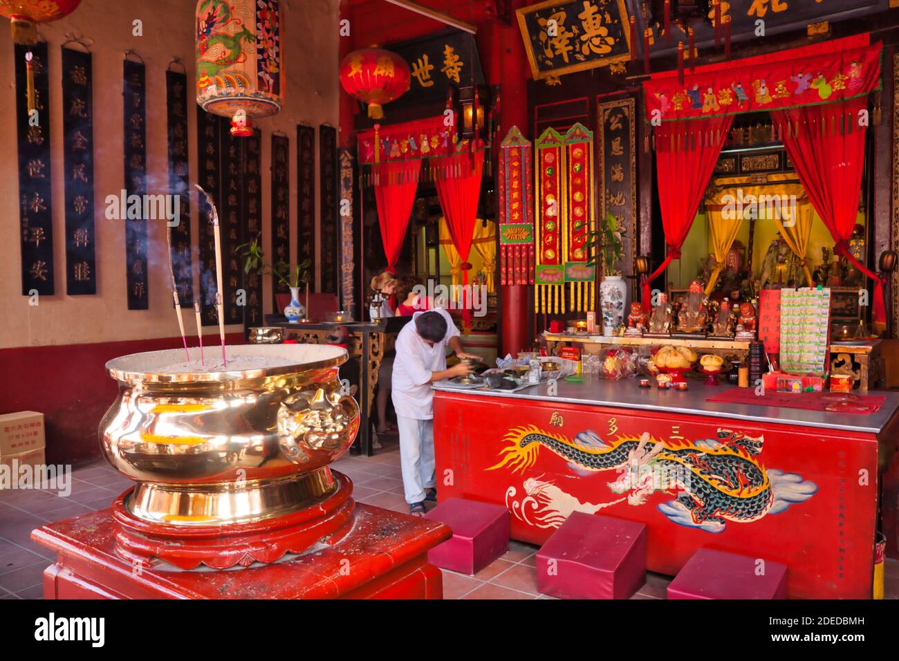 Interni o un tempio cinese a Malacca, Malesia con bastoni di smoking in primo piano e una persona che pulisce Foto Stock