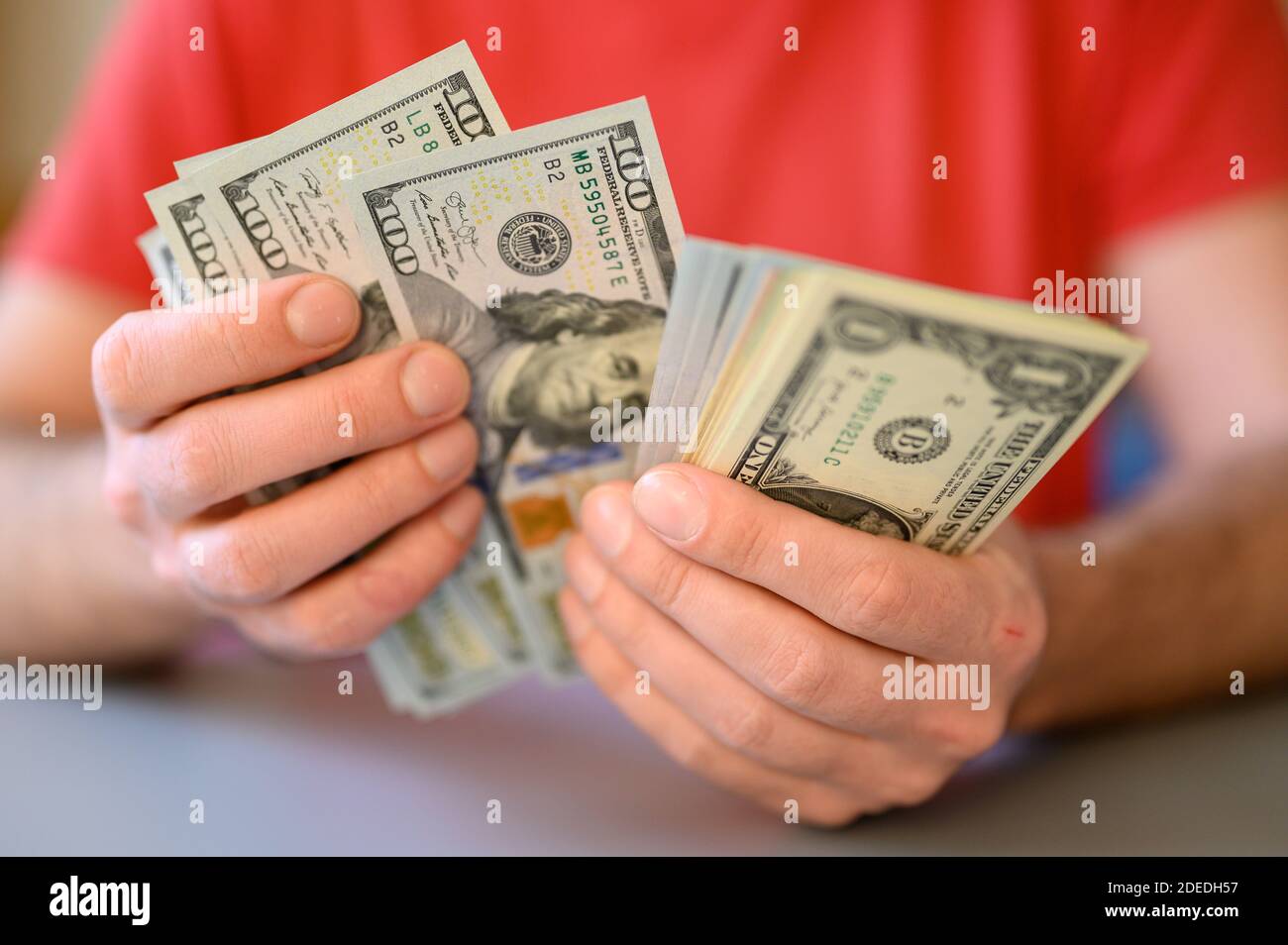 le mani degli uomini tengono e contano 100, 50 e 1 dollaro fatture sulla tabella grigia Foto Stock