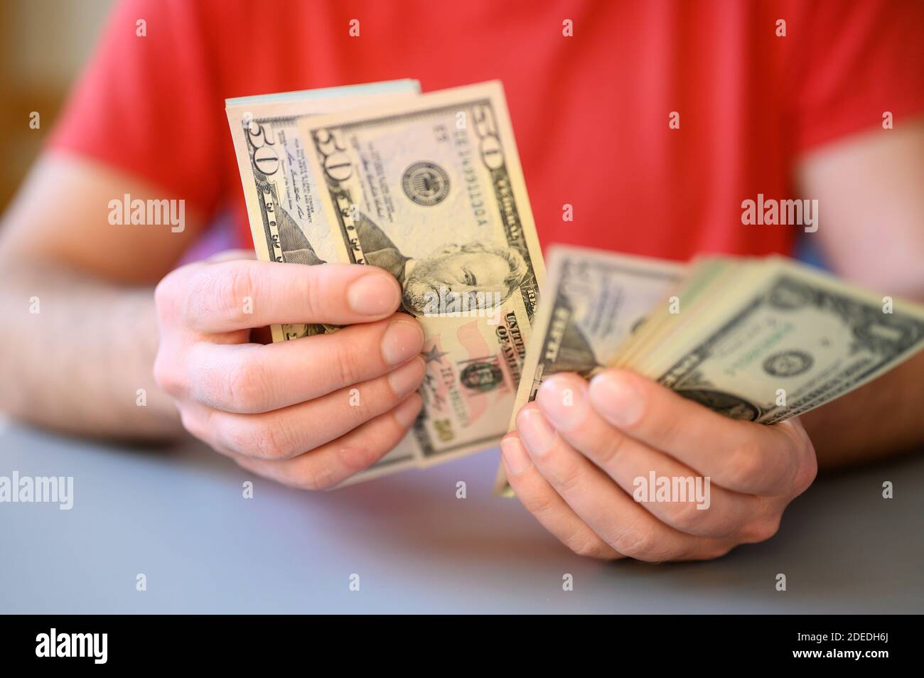 le mani degli uomini tengono e contano 100, 50 e 1 dollaro fatture sulla tabella grigia Foto Stock