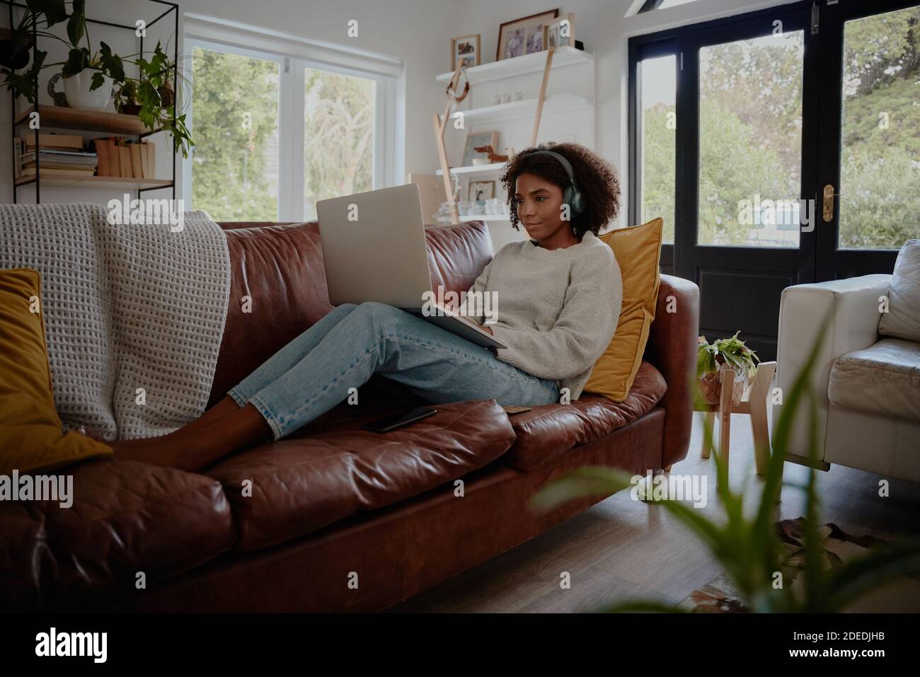 Giovane donna africana che si rilassa sul divano mentre si guarda il film computer portatile con cuffie wireless bluetooth Foto Stock