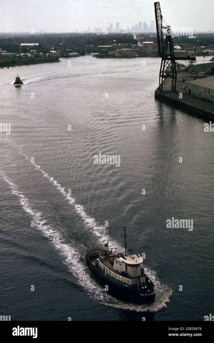 1970 Foto (1973) - Tugs sul canale navale di Houston fortemente industrializzato visto da un ponte di recente costruzione. Sullo sfondo, appena visibile attraverso lo smog, c'è lo skyline di Houston Foto Stock