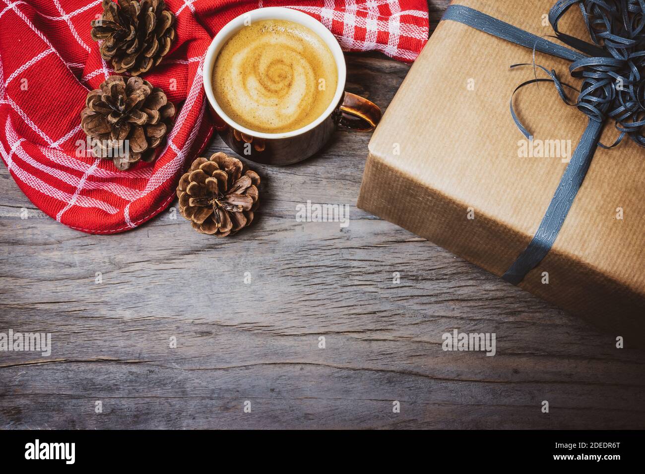 Sfondo natalizio con scatola regalo, tazza di caffè, asciugamano rosso da cucina e coni di pino su rustico tavolo di legno. Foto Stock