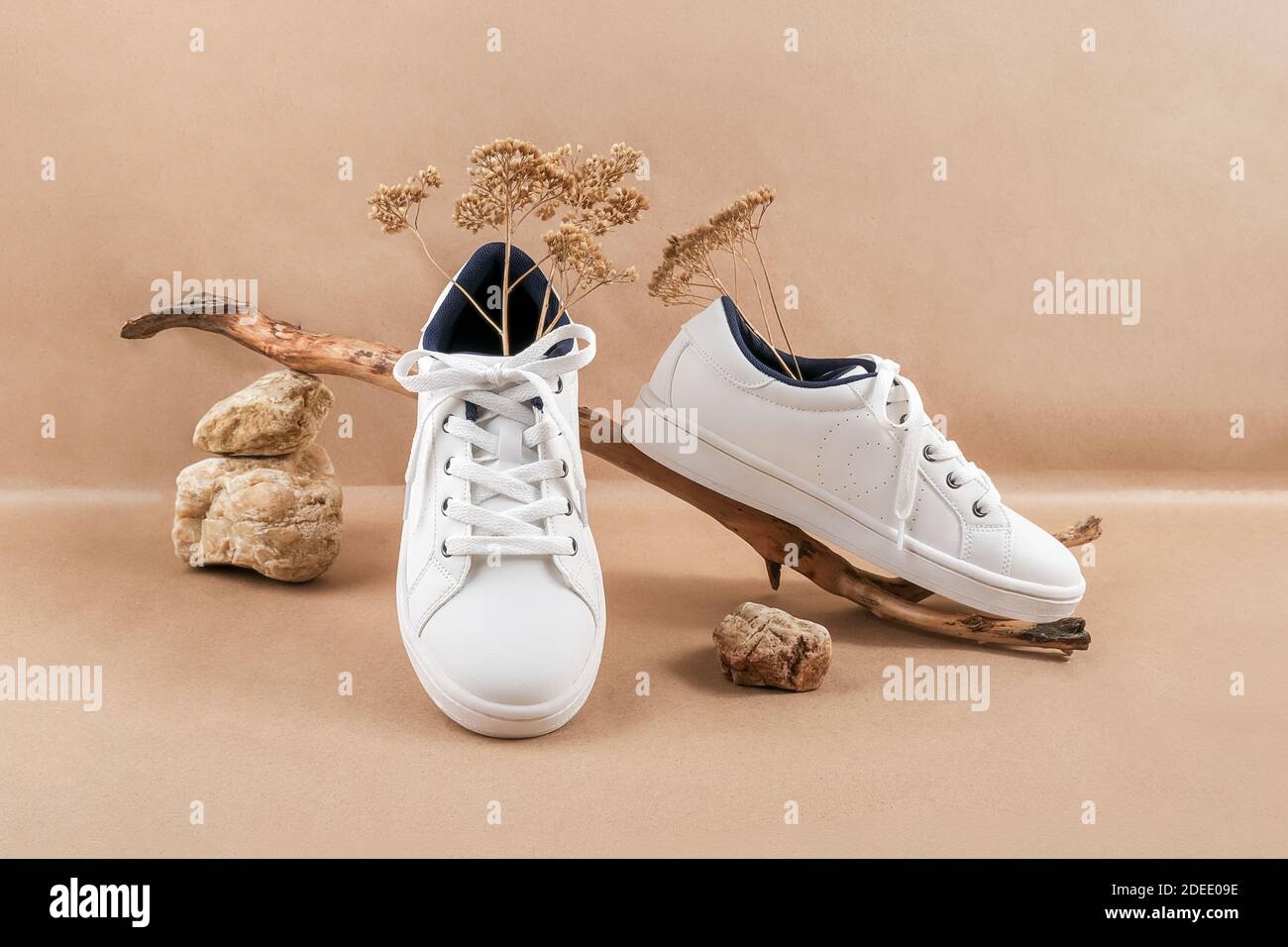 Concetto etico di scarpe vegan. Un paio di sneakers bianche con fiori  secchi sul legno e mucchio di pietre, fondo carta da artigianato beige  neutro Foto stock - Alamy