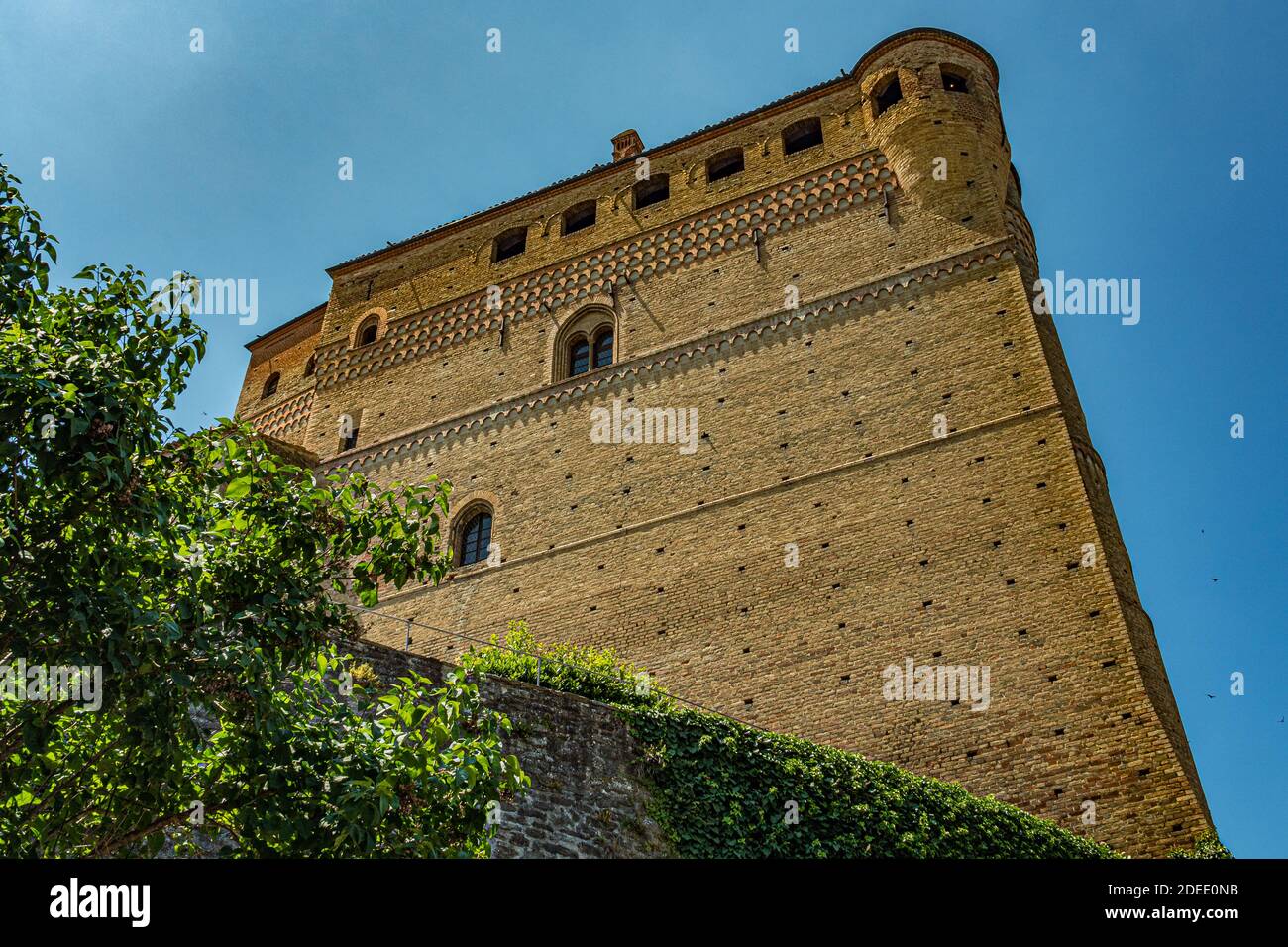 Vista esterna del castello di Serralunga con la torre e le case in mattoni - Città di Serralunga, Italia, Piemonte Foto Stock