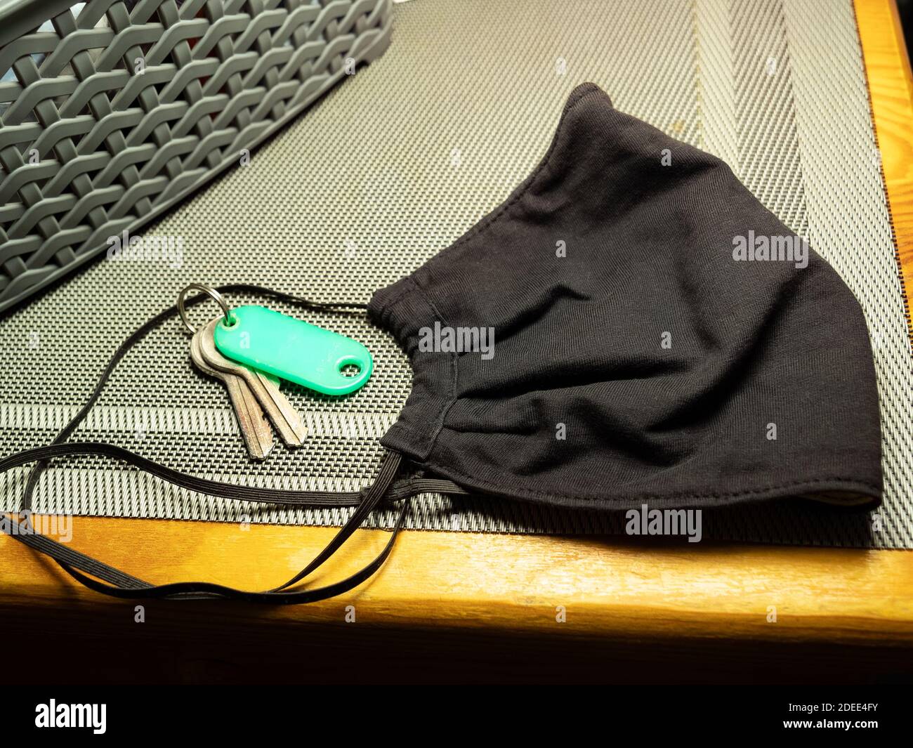 Maschera protettiva anti virale nera semplice e chiavi della casa che si posano sull'armadio. Preparandosi ad abbandonare la vostra casa, dimenticando la maschera nuova normale Foto Stock