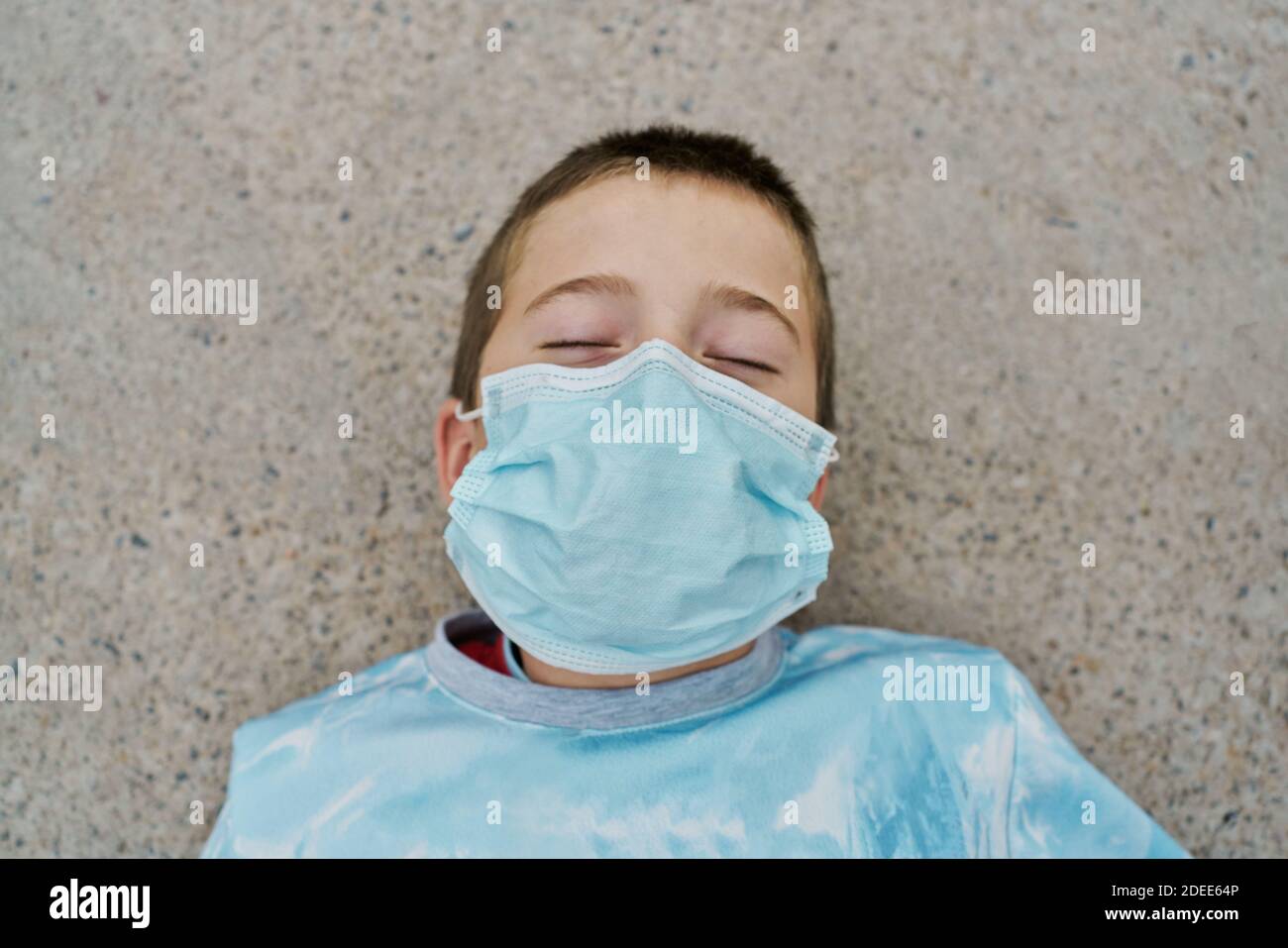 Particolare del ragazzo con maschera protettiva è sdraiato sopra il pavimento e ridendo con gli occhi chiusi Foto Stock