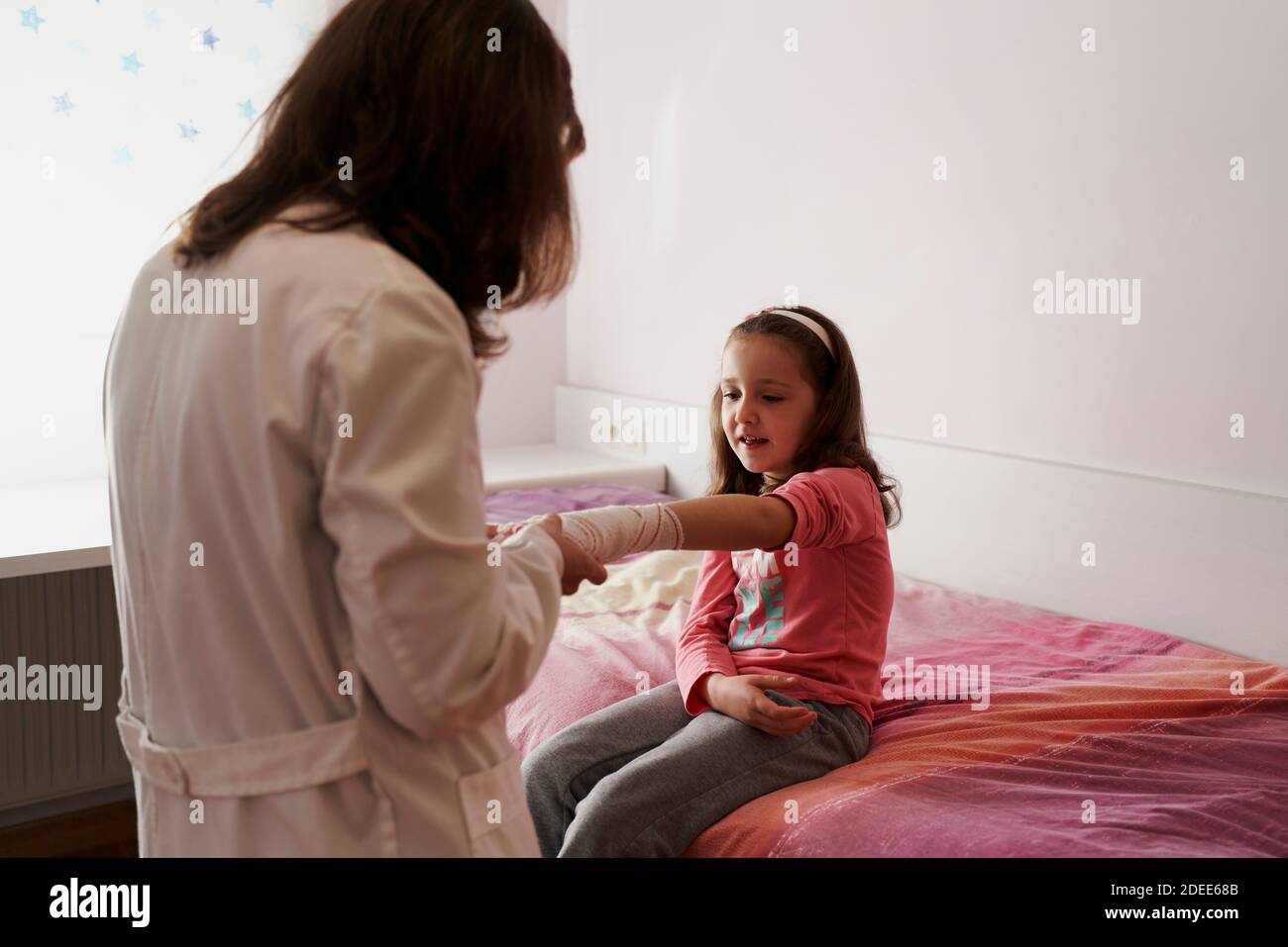 Dottore femmina che bendava il braccio di una bambina nella sua stanza. Concetto medico domestico Foto Stock