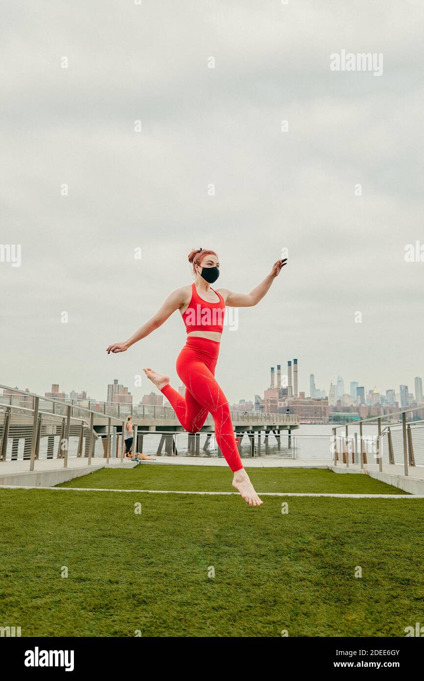 Giovane atleta che salta a mezz'aria indossando la maschera facciale sul lungomare. Foto Stock