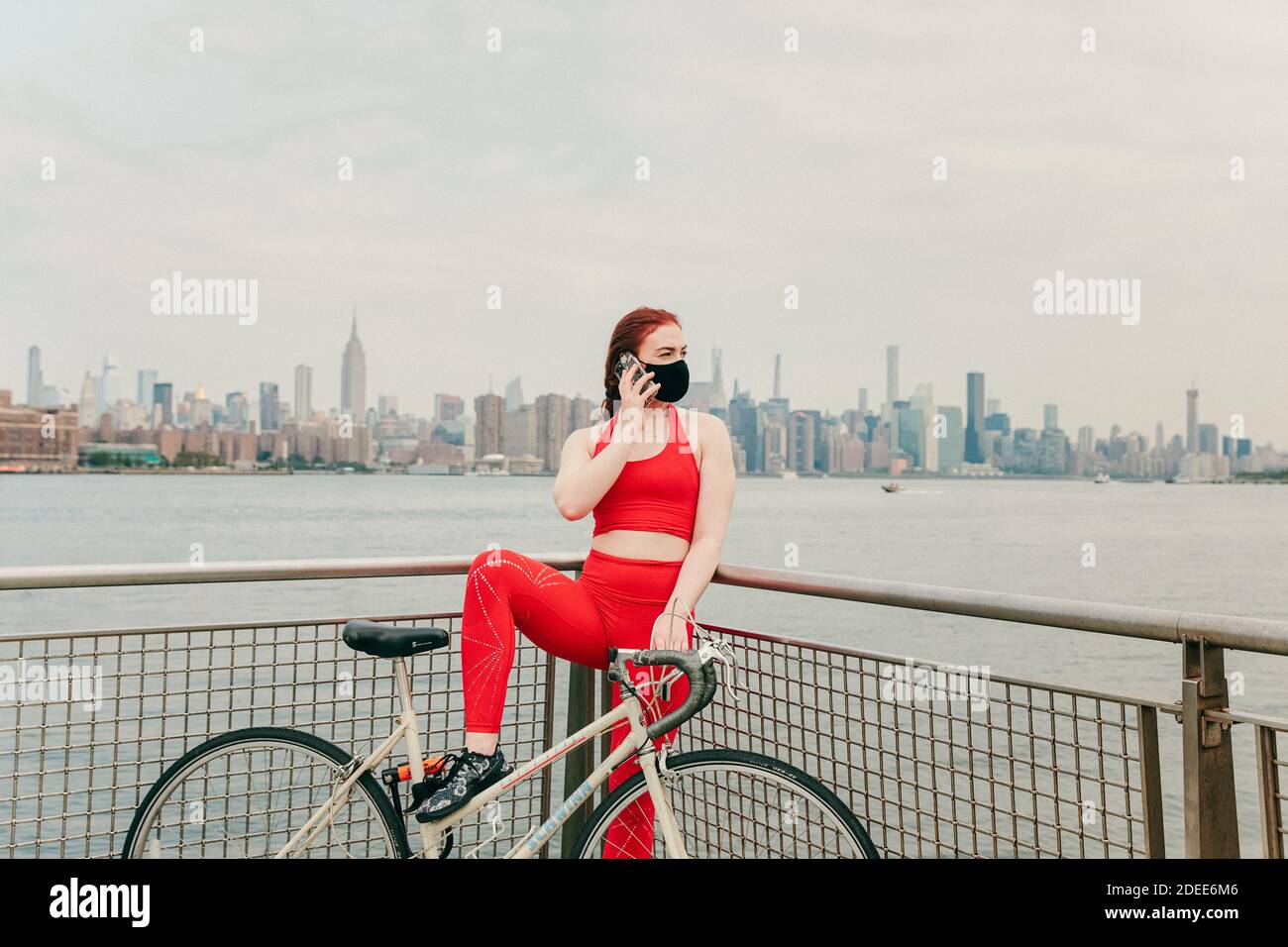 Giovane ciclista femminile che parla al telefono con la moto di Brooklyn lungomare Foto Stock