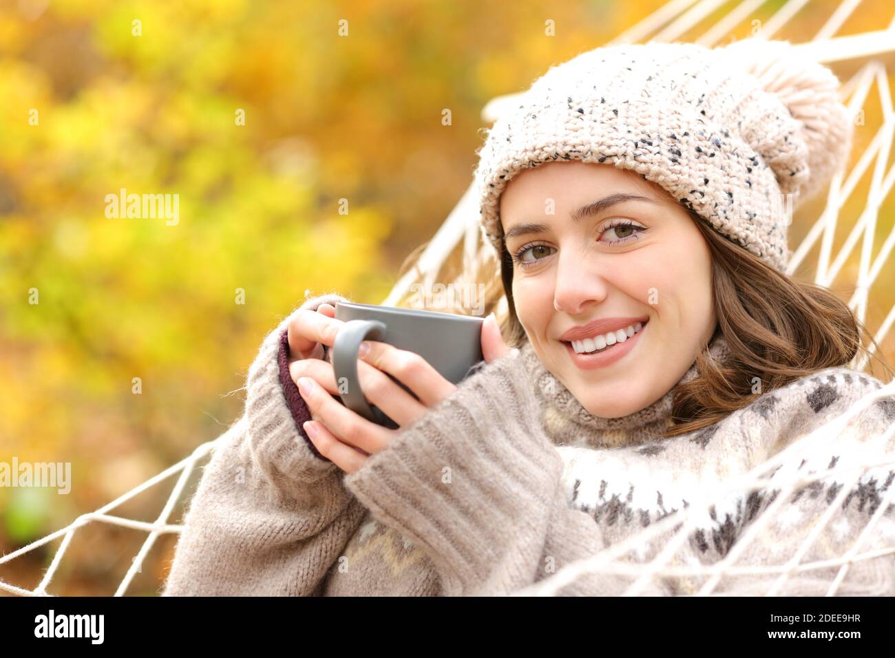 Donna felice che tiene la tazza del caffè che si trova sull'amaca che guarda fotocamera in vacanza autunno Foto Stock