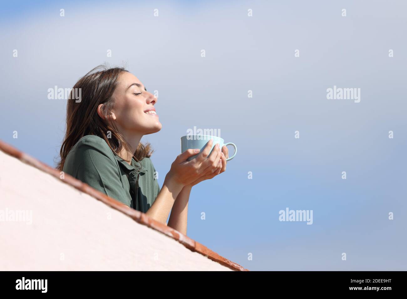 Profilo di una donna felice bere caffè respirando aria fresca dal balcone una giornata di sole Foto Stock