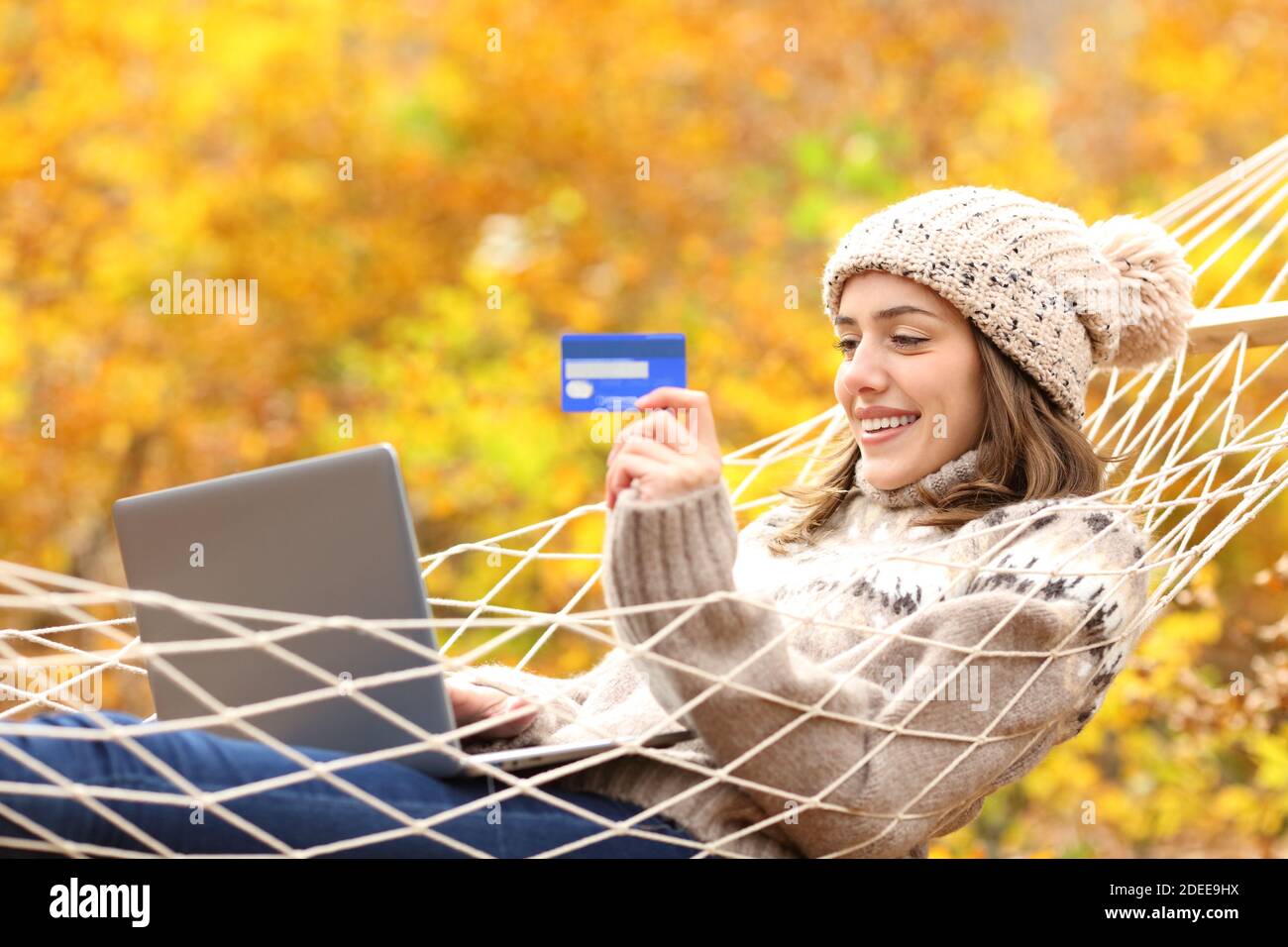 Donna felice di acquistare online con carta di credito e laptop mentendo su amaca in vacanza autunnale Foto Stock