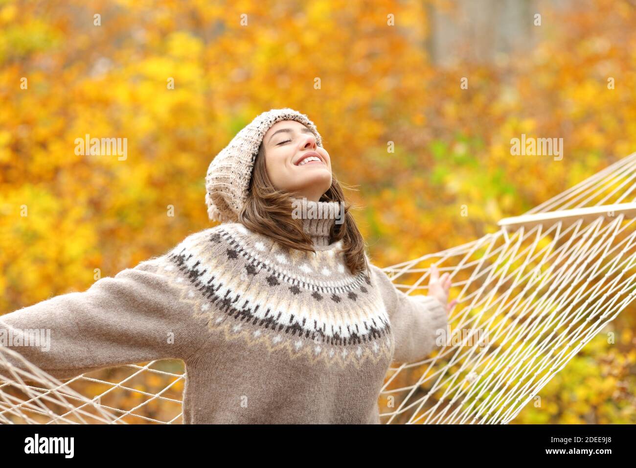 Donna felice seduta su amaca respirando aria fresca che allunga le braccia nella stagione autunnale Foto Stock