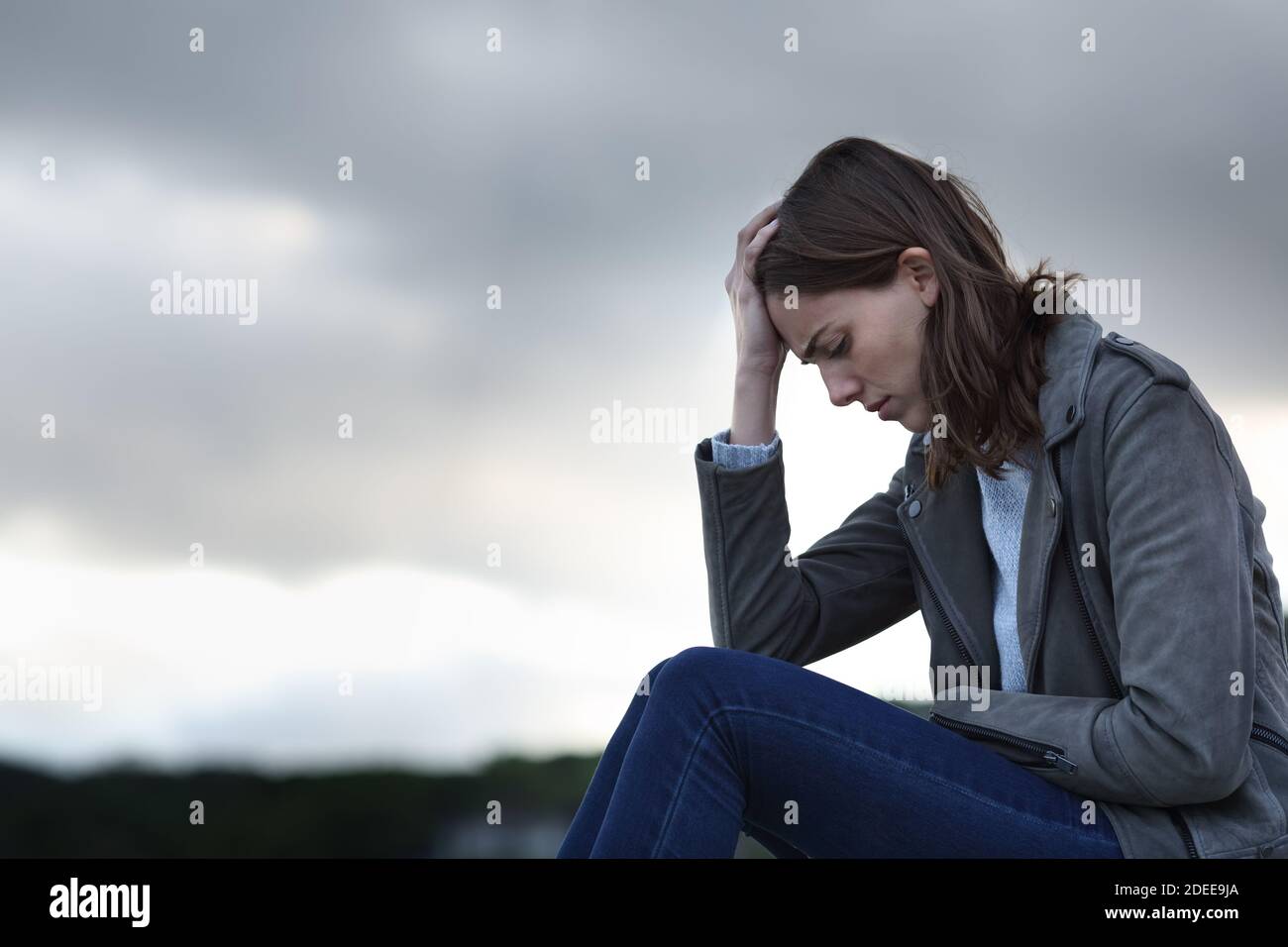 Profilo di una donna triste che lamenta la seduta da sola in un giorno nuvoloso Foto Stock