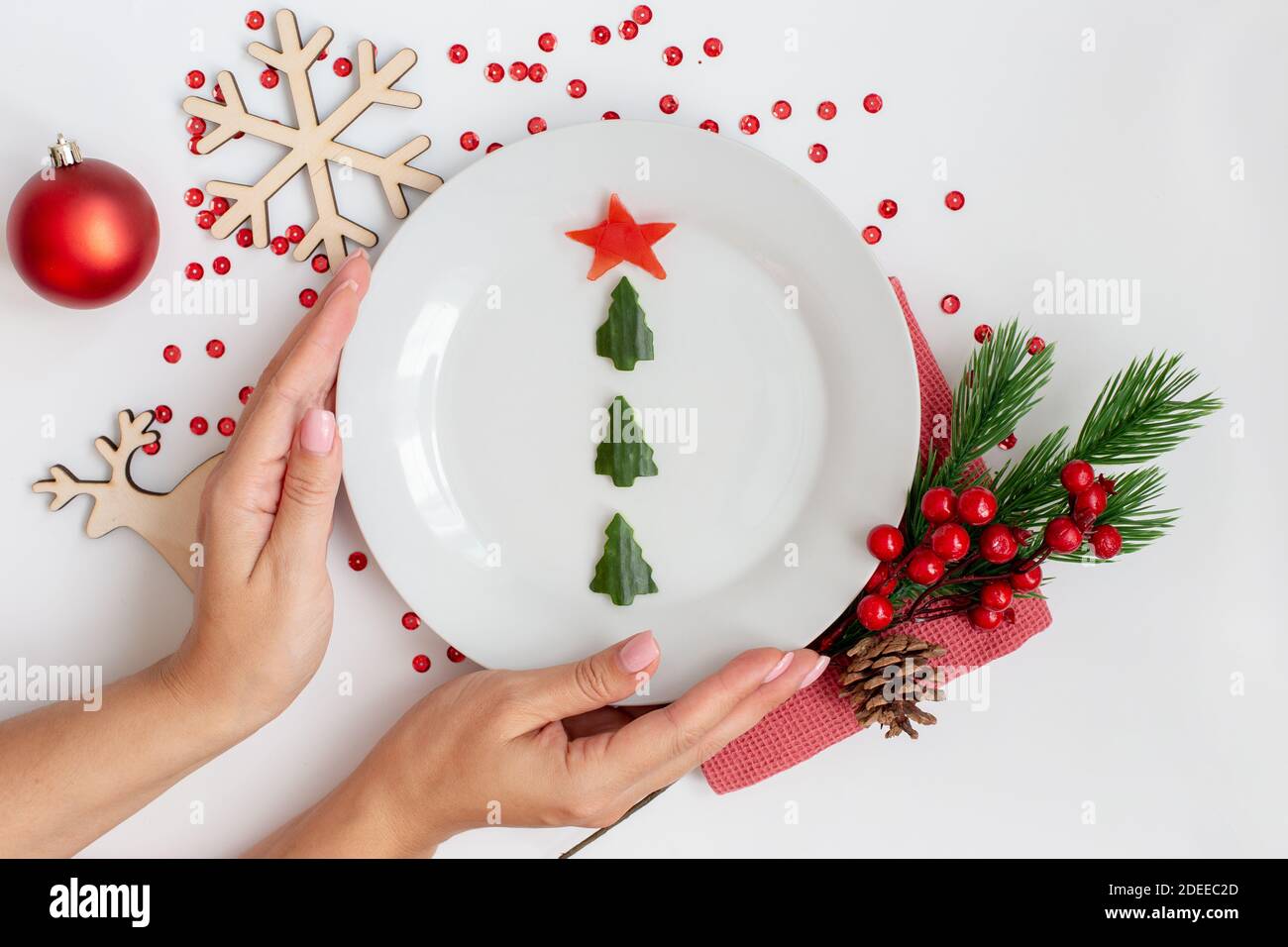 Le mani femminili tengono un piatto bianco con uno spuntino di cetriolo Sotto forma di albero di Natale Foto Stock
