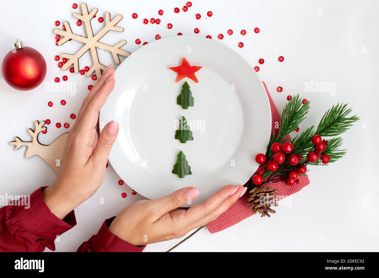 Arredamento del tavolo di Capodanno. Le mani femminili tengono un piatto con uno spuntino di cetriolo sotto forma di un albero di Natale Foto Stock