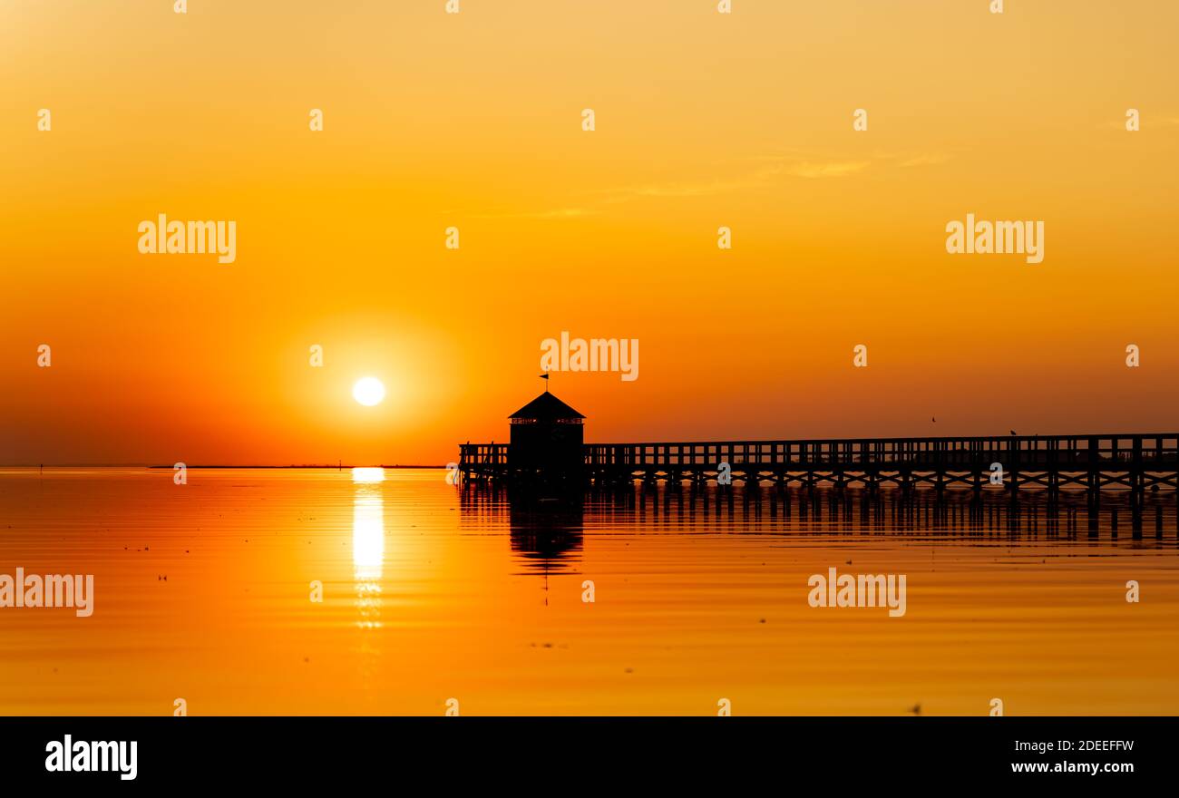 Grande molo in legno su una spiaggia appena bepreponset, ponte è in silhouette nera e il cielo di saturo con calde tonalità arancio dal tramonto. . Alta Foto Stock