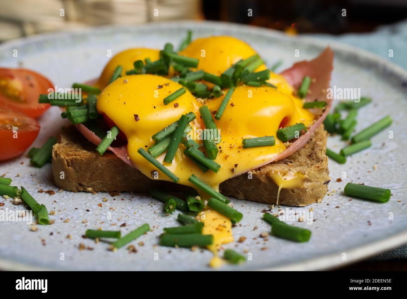 Macro primo piano di pane tostato isolato con prosciutto, erba cipollina, pomodori gratinati con formaggio cheddar fuso su piatto di cina Foto Stock