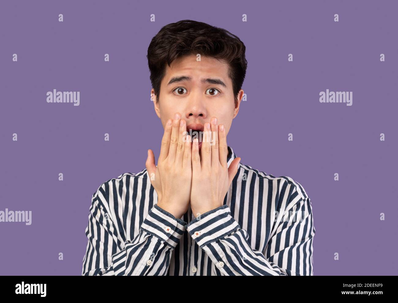 Temuto uomo asiatico grimacing, scioccato in studio viola Foto Stock