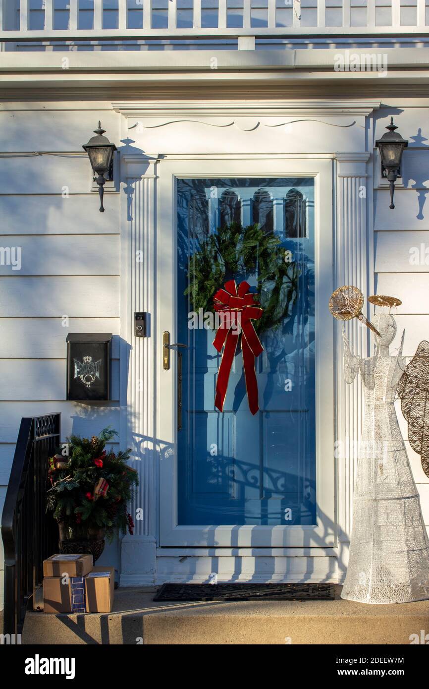 Idea decorazione portico di Natale. Ingresso casa con porta rossa decorata  per le vacanze. Corona rossa e verde di rami di abete e luci sulla  ringhiera. Vigilia di Natale a casa Foto