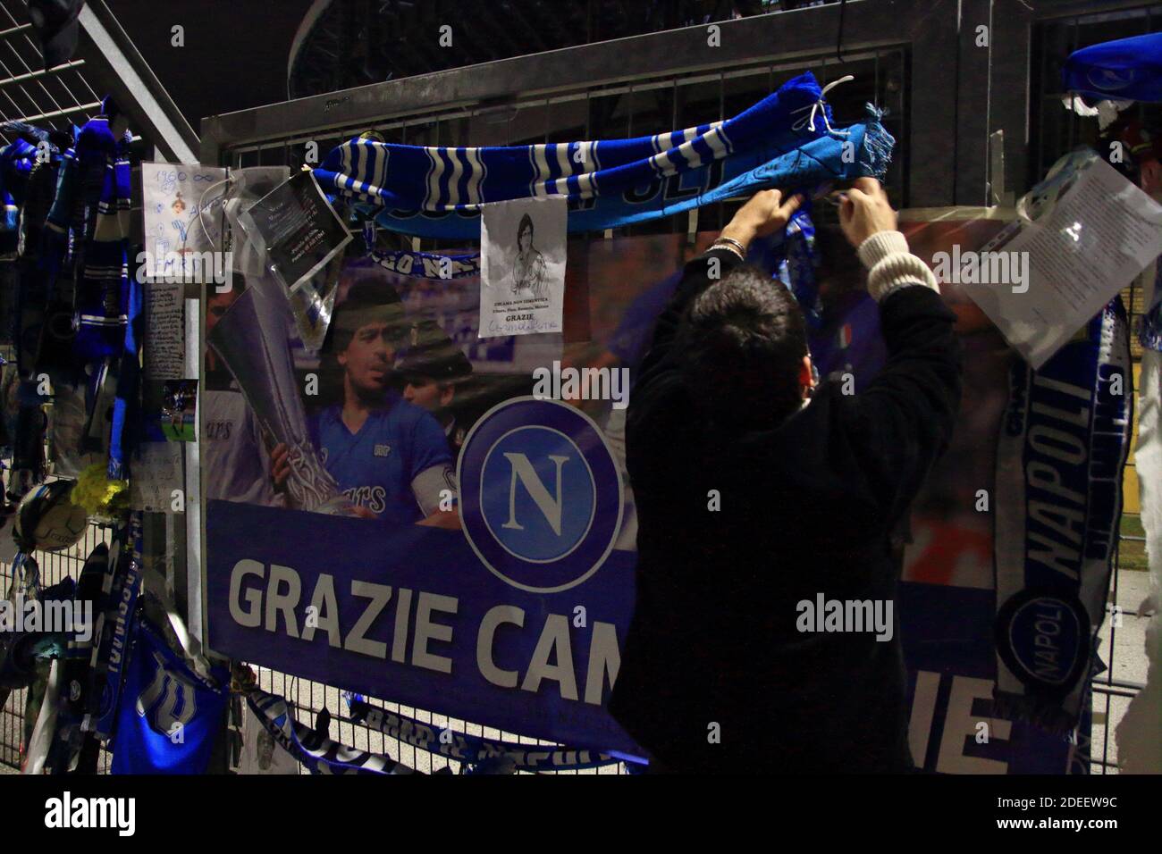 Un fan mette una sciarpa di Napoli in memoria di Diego Armando Maradona davanti alle porte dello Stadio San Paolo , nei giorni successivi alla morte Foto Stock