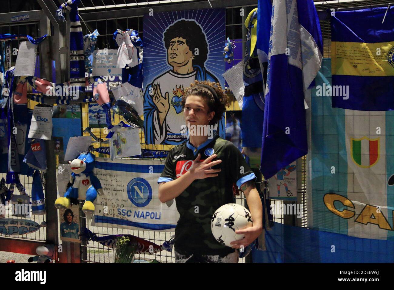 Un giovane fan di Napoli in posa per la foto ricordo con camicia e palla davanti ai cancelli del Stadio San Paolo pieno di oggetti lasciati dai fan di Napoli Foto Stock