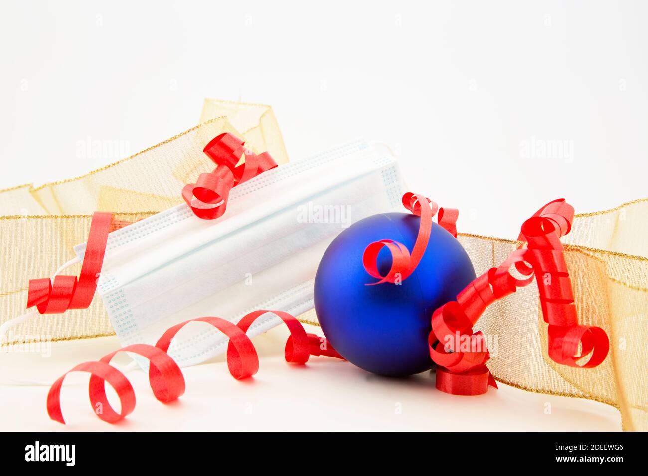 Palla di festa blu e oro e arricciati; nastri rossi con maschera medica riflettono la necessità di protezione personale durante la crisi Covid e stagione di festa attiva Foto Stock