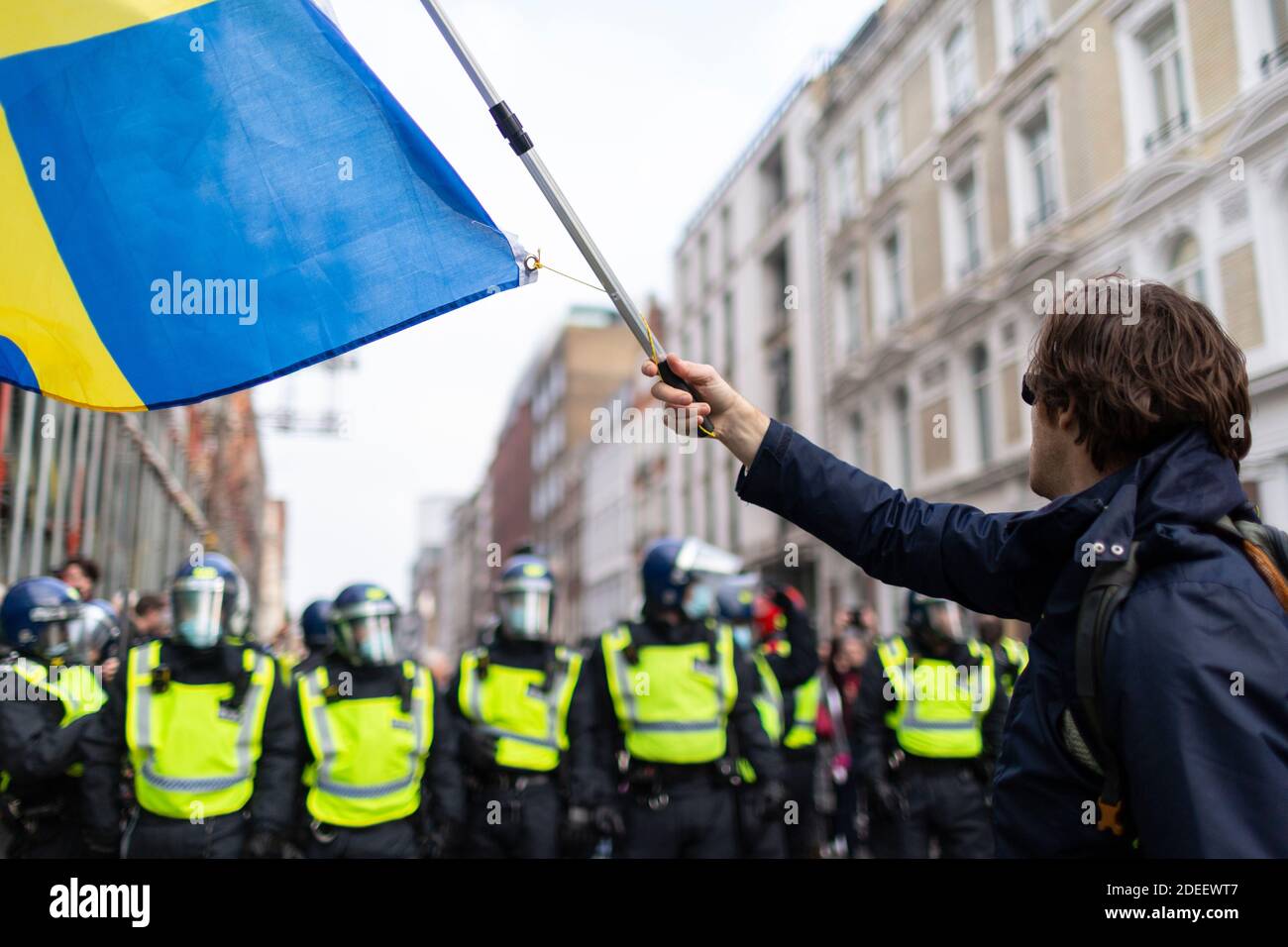 Protesta anti-lock-down, Londra, 28 novembre 2020. Un protetore ondeggia una bandiera di fronte a una fila di ufficiali di polizia in attrezzatura da rivolta. Foto Stock