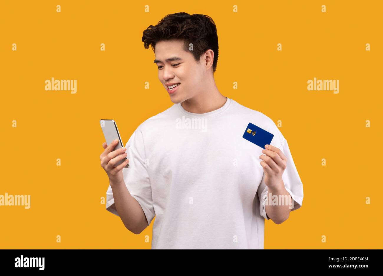 Ragazzo asiatico che detiene carta di credito e cellulare in studio Foto Stock