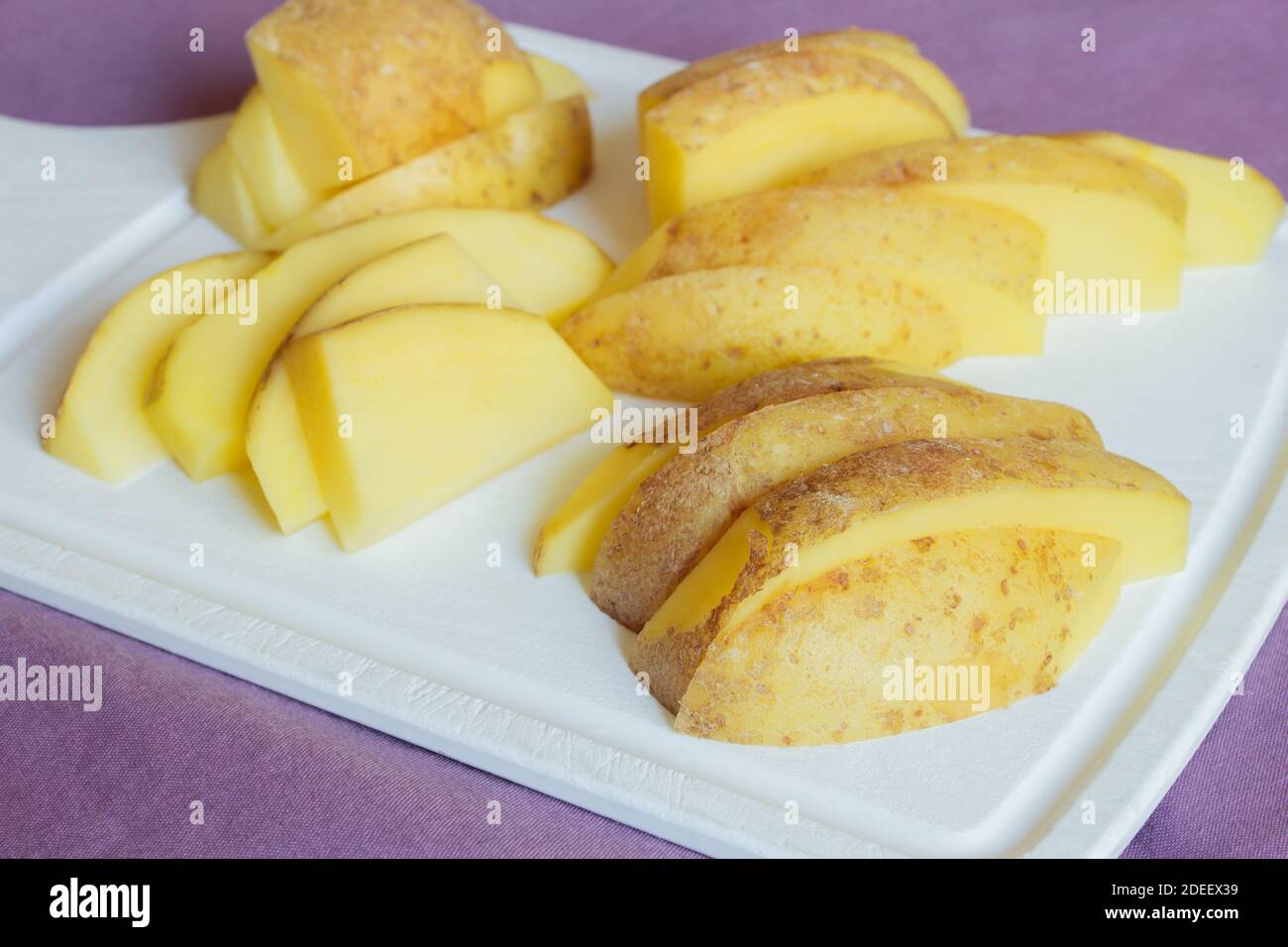 Patate appena tagliate preparate con spezie per il forno su un tagliere da cucina. Cibo sano e vegano. Foto Stock