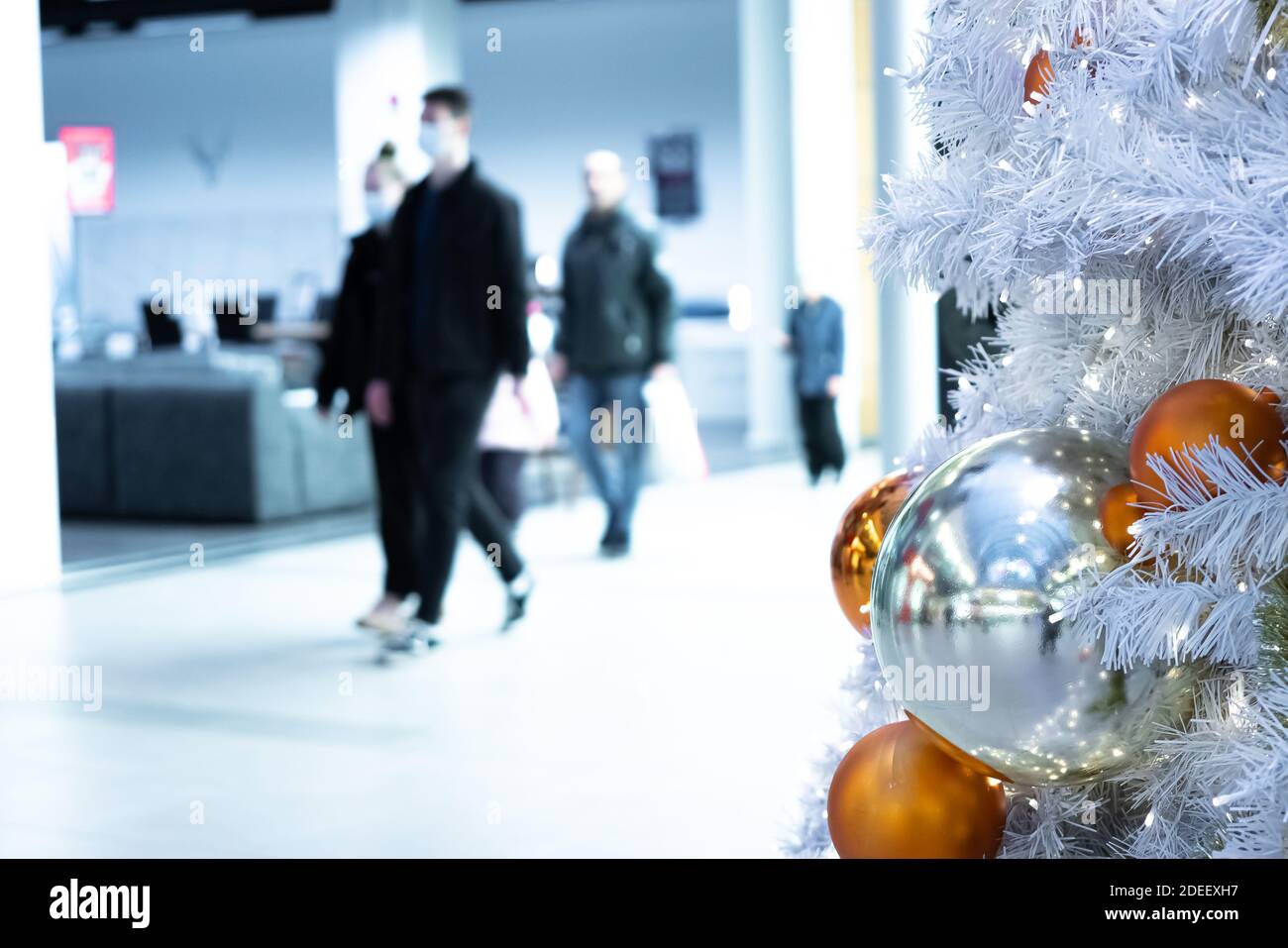 Grandi, belle palle di Natale su un albero di Natale bianco e su uno sfondo sfocato persone in maschere mediche. Concetto , Proteggiti dal virus corona nei luoghi pubblici. Incontro natale, nuovo voi. Foto di alta qualità Foto Stock