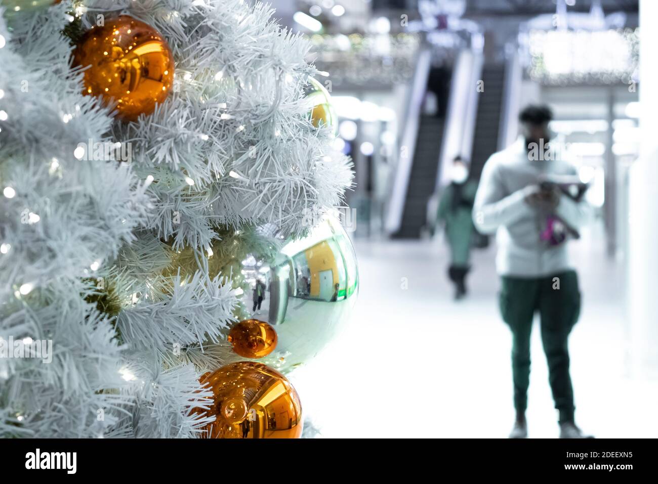 Grandi, belle palle di Natale su un albero di Natale bianco e su uno sfondo sfocato persone in maschere mediche. Concetto , Proteggiti dal virus corona nei luoghi pubblici. Incontro natale, nuovo voi. Foto di alta qualità Foto Stock