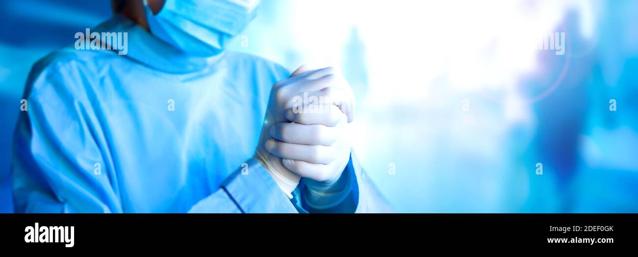 Frontline giovane donna stanca medico indossando guanti sterili. Indossare maschera medica protettiva e uniforme blu. Le mani si avvicinano. Ampio banner con spazio di copia - salute, medicina e pandemia. Foto Stock