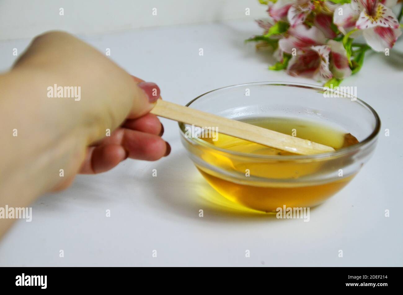Immagine di zucchero liquido per capelli rimozione cera depilazione vaso di vetro di miele dorato chiodo di garofano con fiori di frangipani. Preparazione del trattamento naturale del corpo di bellezza Foto Stock