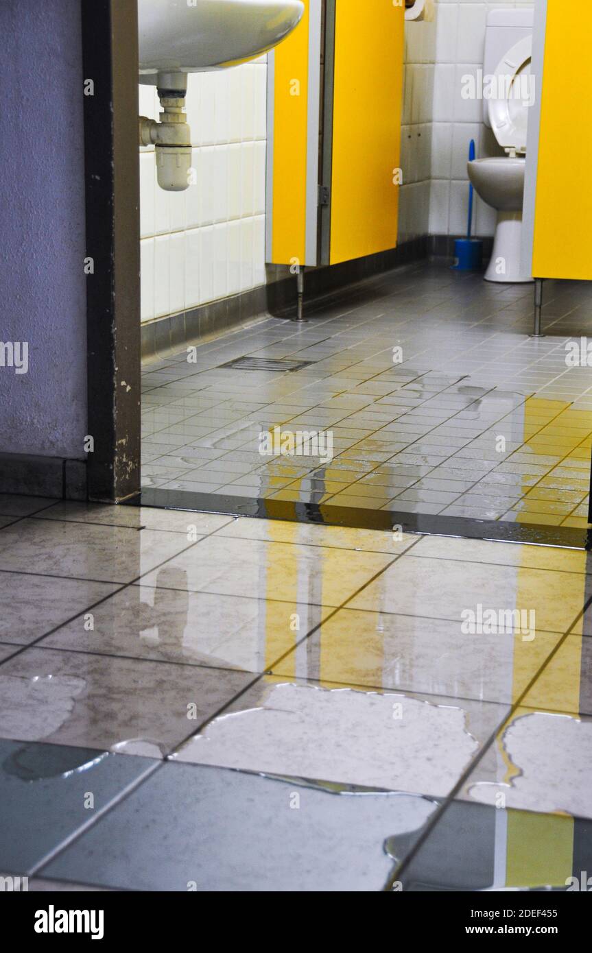 Pozze d'acqua sul pavimento piastrellato di un aeroporto pubblico bagno / toilette. Alluvione. Alluvione da tempesta. Foto Stock